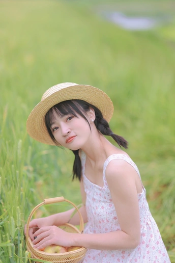 一个戴着草帽的年轻女子坐在绿草地上 手里拿着一个装满苹果的篮子。