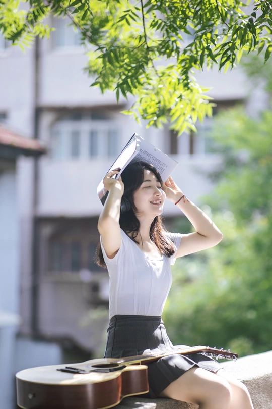 一个戴帽子坐在墙上弹吉他并看书的女青年