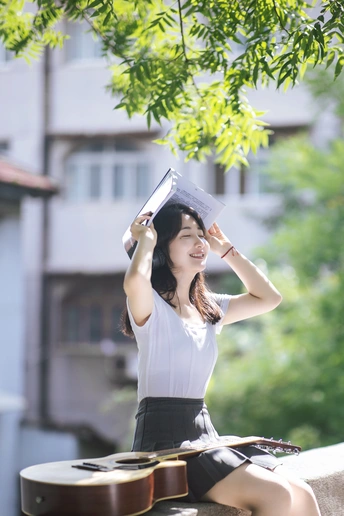 一个戴帽子坐在墙上弹吉他并看书的女青年