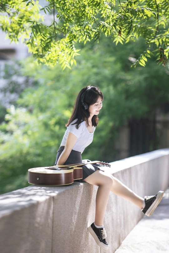 一个年轻女子坐在墙上 带着一个手提箱和一把吉他。