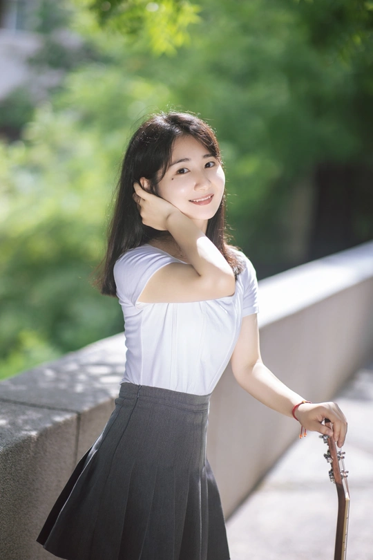 一位穿着白色连衣裙的年轻女子站在墙边 手里拿着一把雨伞。