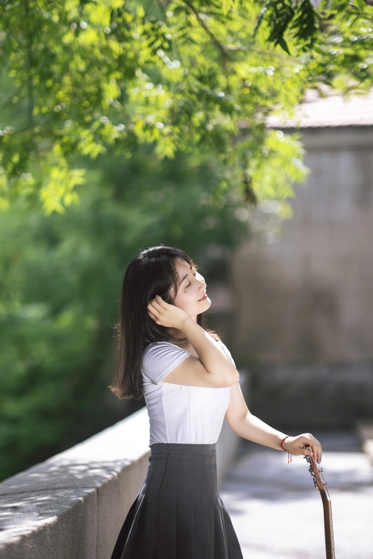 一位穿着白色连衣裙的年轻女子手持一根木棍和一把黑色雨伞站在桥上