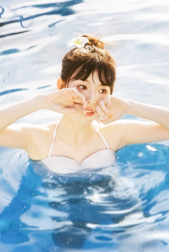 一位穿着比基尼的年轻女子在蓝色游泳池中摆姿势