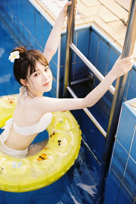 一位年轻女子站在一个漂浮的环上 游泳池中 有梯子和黄色管。