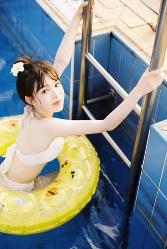 一位年轻女子站在一个漂浮的环上 游泳池中 有梯子和黄色管。