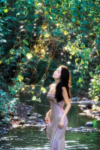 站在河里或小溪里的一位身穿粉色连衣裙的美丽年轻女士