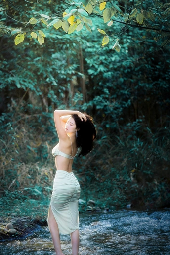 一位身穿白色连衣裙的美丽年轻女士站在森林中的溪流中