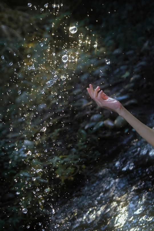 年轻女子在瀑布或小溪边的水中玩耍 小男孩伸出手去触摸泡泡