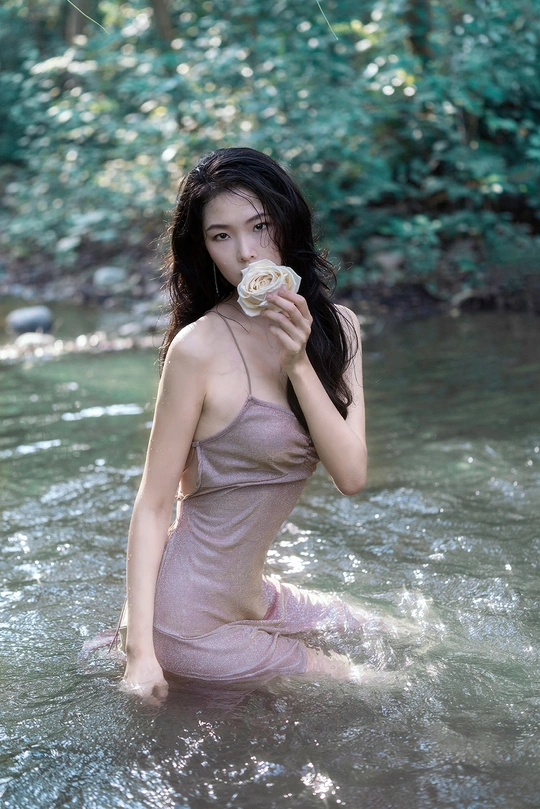 一个穿着漂亮连衣裙的年轻女子在河里拿着一朵花