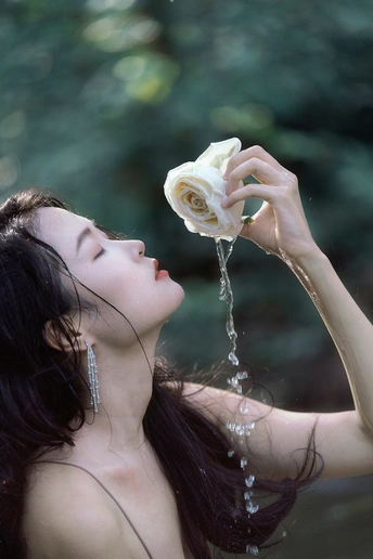一个美丽的年轻女子拿着一朵白玫瑰向她喷水