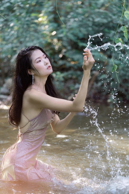 一个穿着粉色连衣裙的年轻女子在河里或小溪里泼水