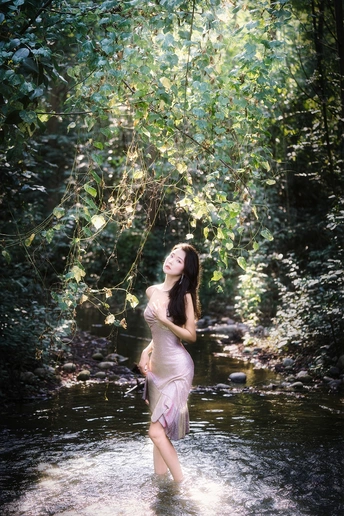 一个穿着漂亮飘逸连衣裙的年轻女子站在树林里的河里或小溪里