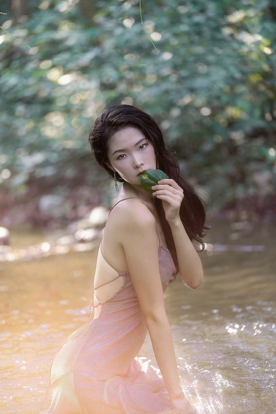 一个穿着粉色连衣裙的美丽年轻女子在河里拿着一片绿叶