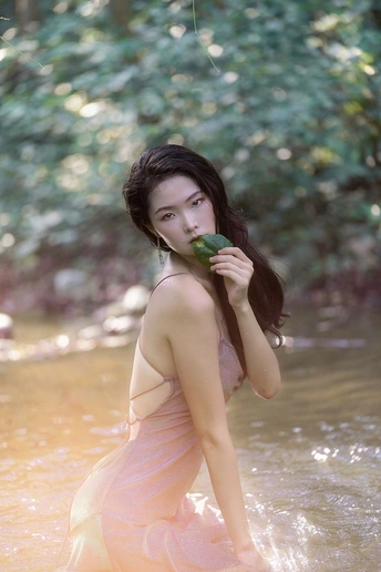 一个穿着粉色连衣裙的美丽年轻女子在河里拿着一片绿叶