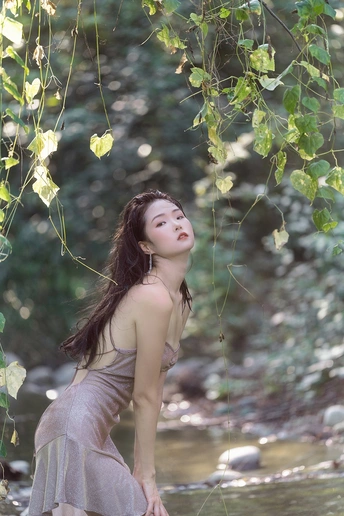一个穿着漂亮连衣裙的年轻女子站在森林里的小溪里