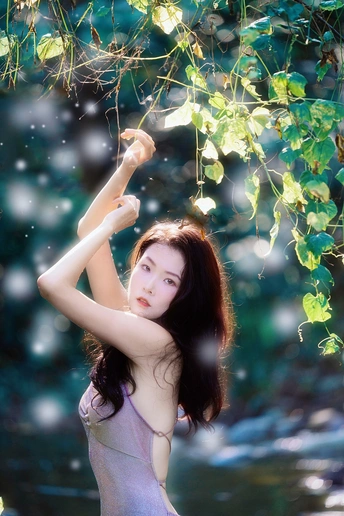 一位穿着漂亮连衣裙的年轻女子在河边的森林里摆姿势