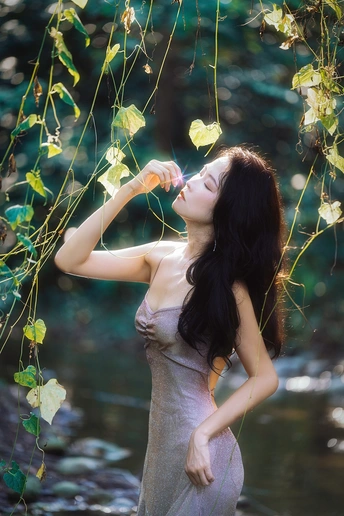 一个穿着漂亮连衣裙的年轻女子拿着一个从小溪或河里喝水的瓶子