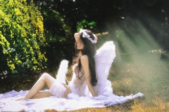 一个坐在草地上毛毯上的有白色羽翼的年轻女子