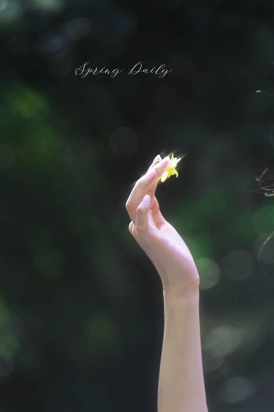 一个小女孩手里拿着一朵黄色的小花 背景模糊 绿色背景在她的手指后面。
