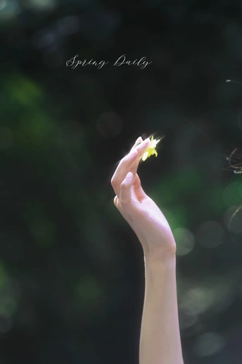 一个小女孩手里拿着一朵黄色的小花 背景模糊 绿色背景在她的手指后面。