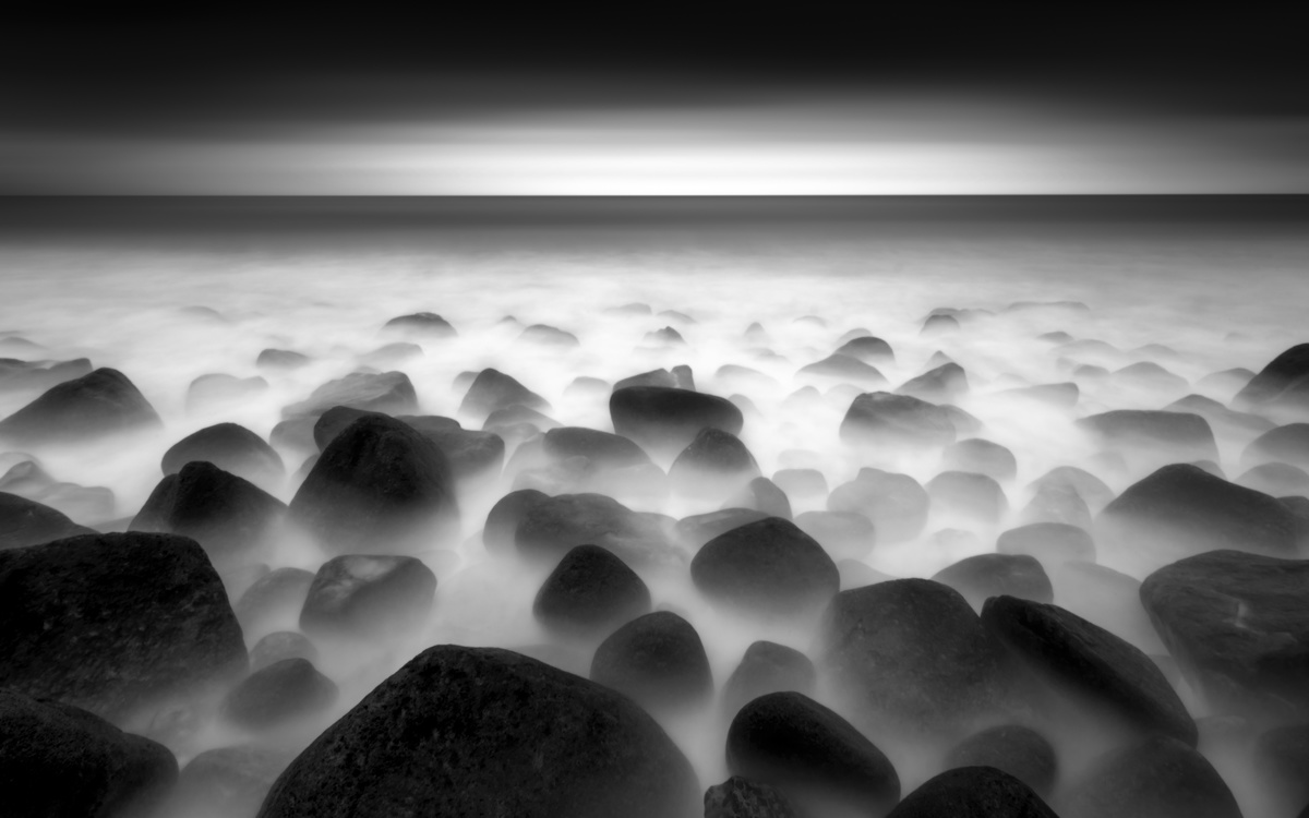 黑白长曝光海滩上有岩石和水中的雾气在天空中