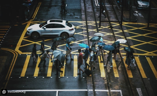 人们打着伞穿过人行横道 街上有一辆车。