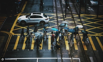 人们打着伞穿过人行横道 街上有一辆车。