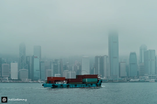 雾中 城市前方有一大片水域 背景中有摩天大楼 前景中有小船。