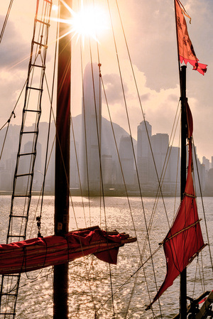 一艘带有红色风帆和旗帜的帆船 停泊在港口 背景是一座大型城市。