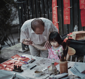 一个老人在一个桌子旁帮助一个年轻女孩画画。