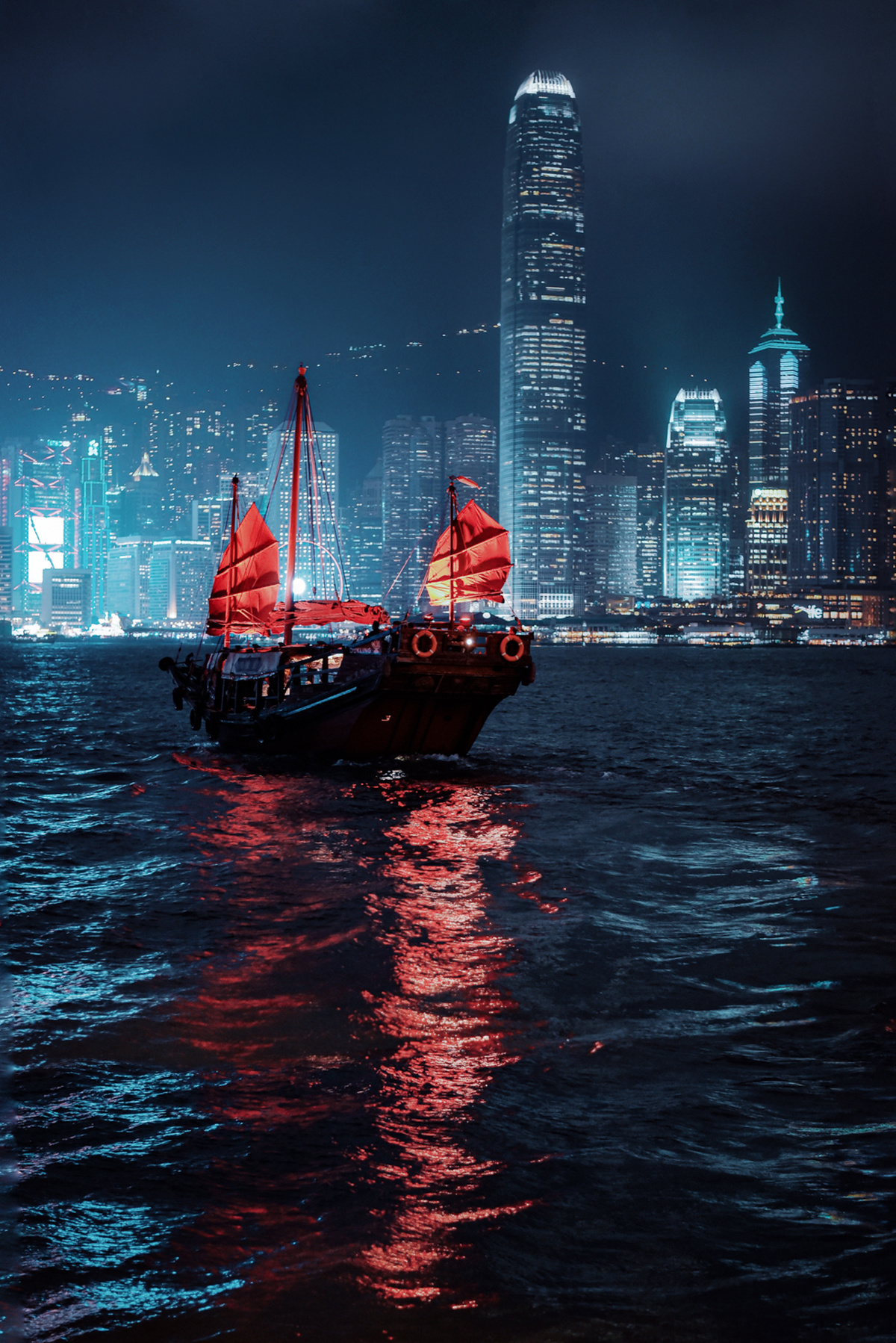 夜晚在大城市前方漂浮着一艘大船 船上有红色的帆。