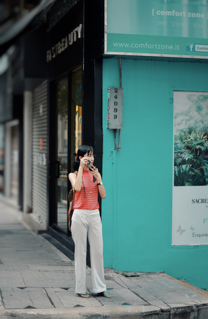 一位穿着格子衬衫和裤子的女人站在一栋建筑物的 sidewalk 上 用她的相机拍照。