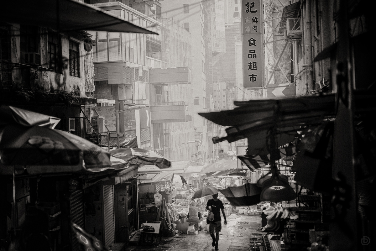 一张黑白照片 展示了一个亚洲城市的巷子 人们手拿雨伞走在街道上。