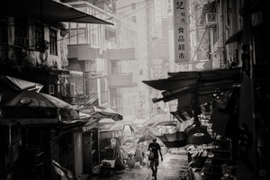 一张黑白照片 展示了一个亚洲城市的巷子 人们手拿雨伞走在街道上。