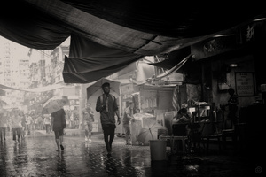一张黑白照片 一个男子在雨中持伞在城市中行走。