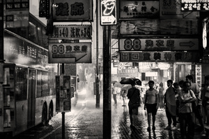 一张黑白照片 展示人们在雨中行走 在一个亚洲城市的湿漉漉的人行道上夜晚。