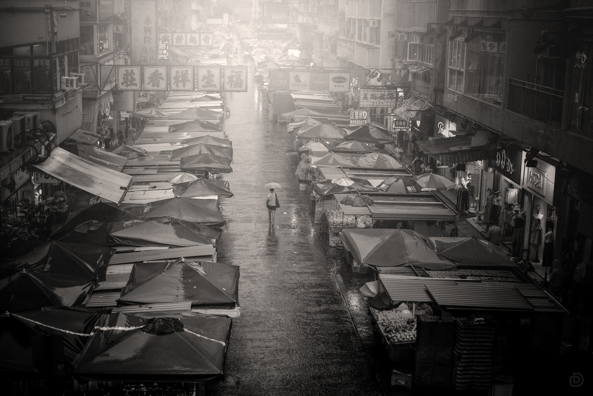 一张黑白照片 许多人沿着街道走 带着伞。
