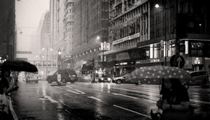 一张黑白的城市夜景照片 人们打着伞在雨中行走。