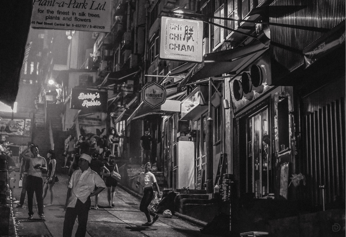 一张黑白照片 展示人们在亚洲城市的一条小巷中行走。