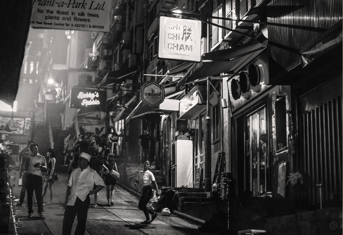 一张黑白照片 描绘了城市中人们沿着小巷行走的场景。