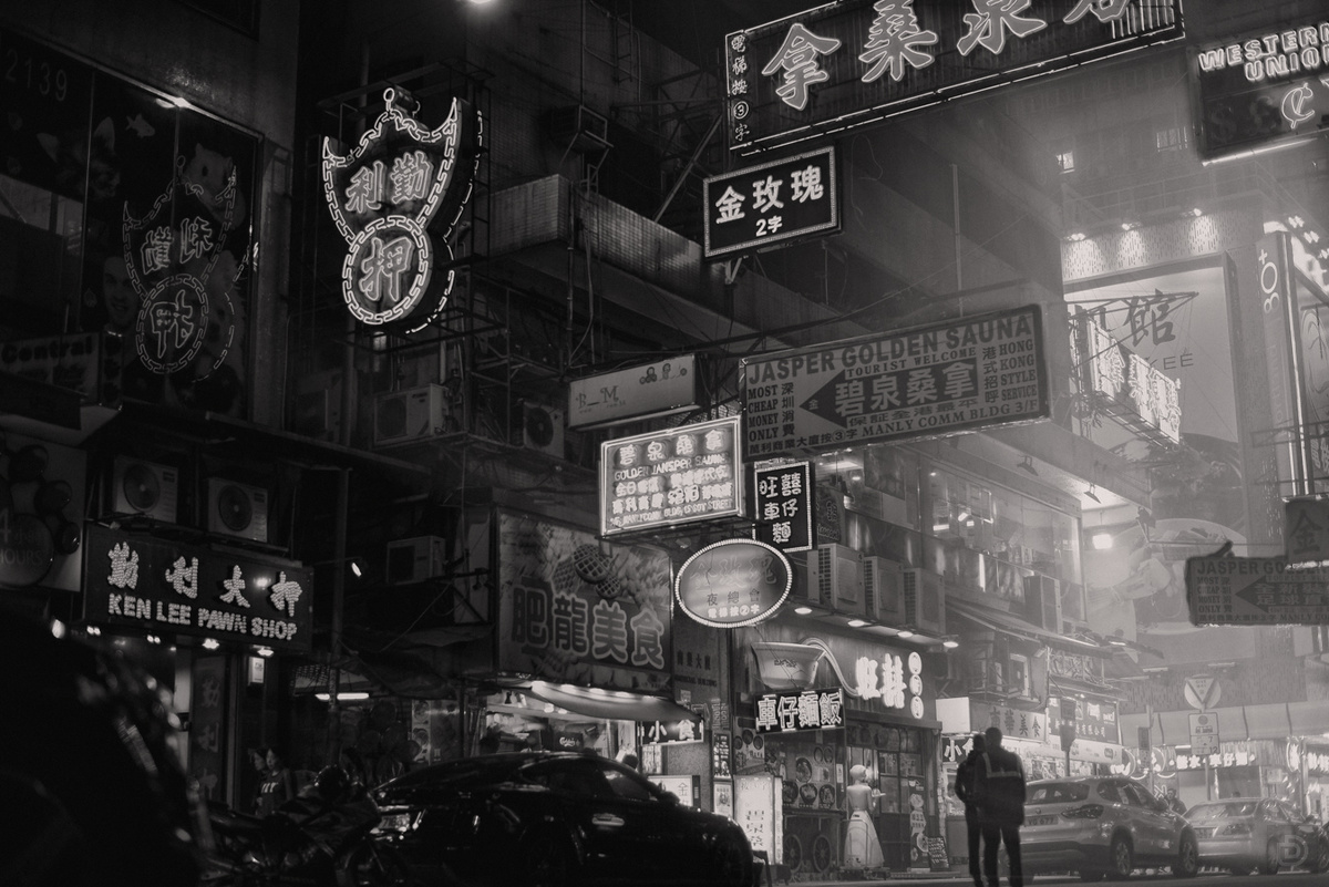 一张黑白照片 展示了一个亚洲城市的夜晚 有人们在走 有汽车 有建筑 还有标志。