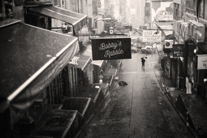 一张黑白照片 展示了一个城市中的狭窄小巷 一个人正在街上走 手里拿着一把伞。