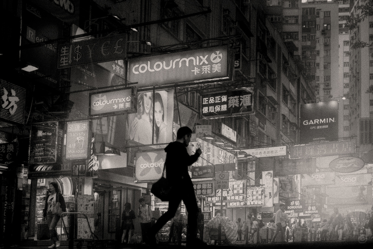 一个夜晚 一个穿着黑白衣服的女人走在一条黑暗的街道上 而一个男子正在玩手机。