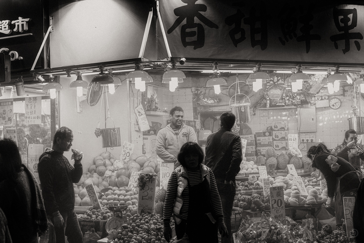 一张黑白照片 人们站在一家售卖水果和蔬菜的商店前。