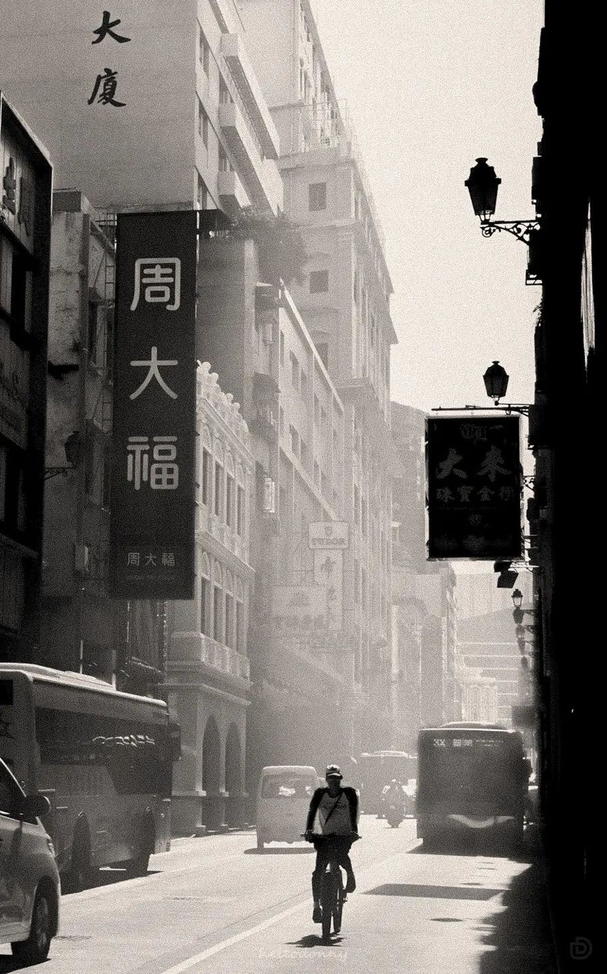 一张黑白照片 画面中有建筑物、汽车和一个人骑自行车穿过街道。