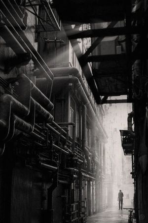 一个穿着黑色衣服的男子在工业建筑的黑暗小巷中行走