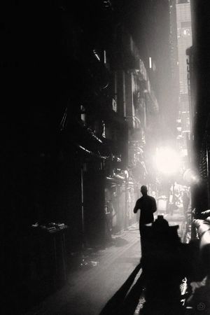 夜晚的黑暗城市 一名男子走在黑暗的巷子里 周围有建筑和汽车。