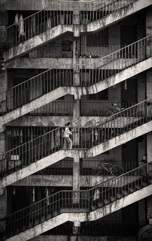 黑白照片 一座老建筑 一位女士站在楼梯上 一位男士骑自行车。