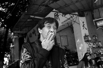 一个男子站在桌子前 手里拿着烟 对着嘴。