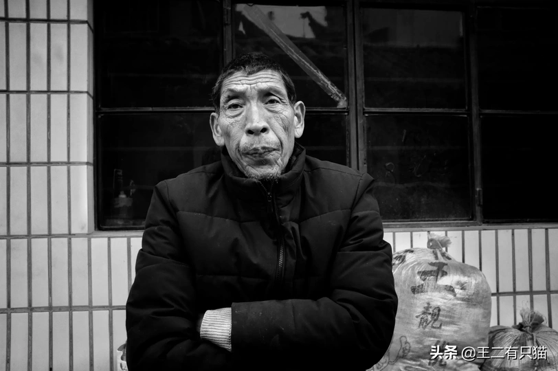 一位老人站在一栋建筑前 手里拿着一个袋子。